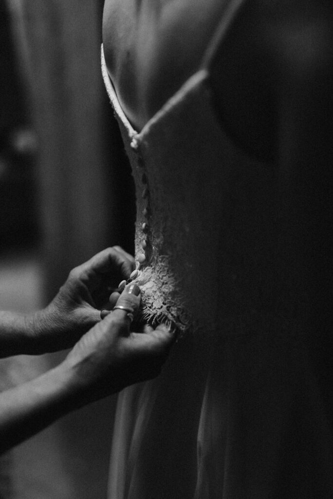 Close up of mother buttoning brides wedding dress in black and white