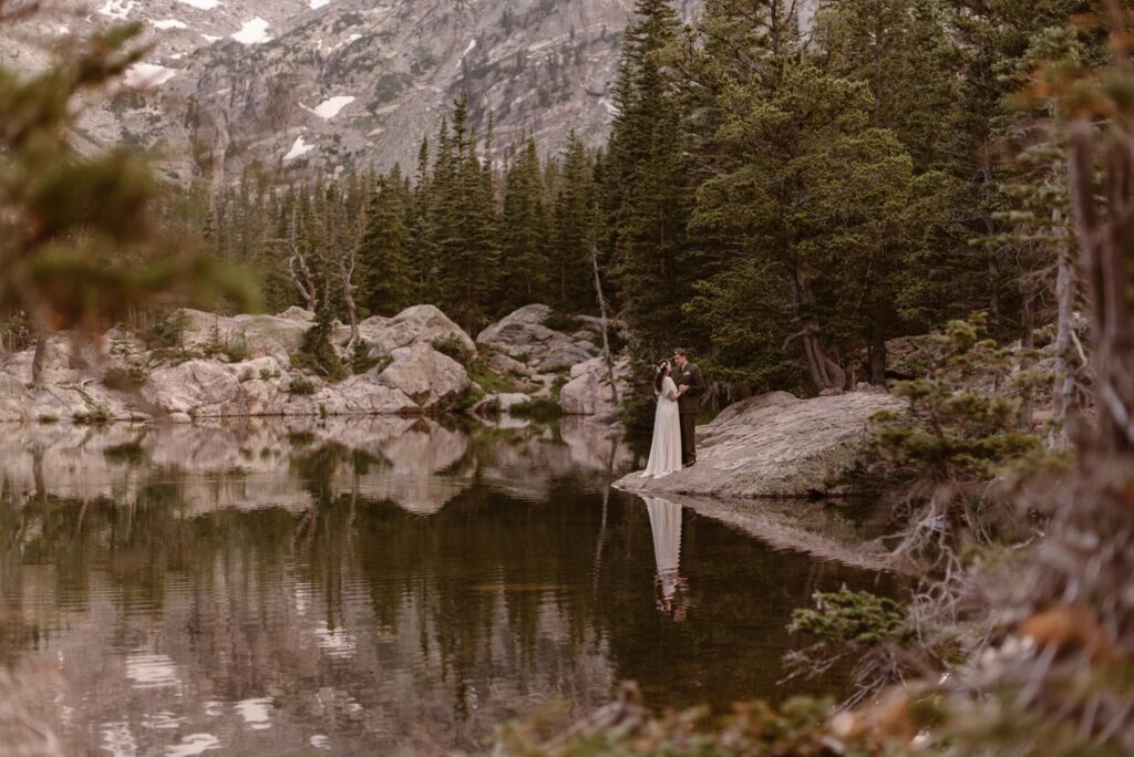 Bride and groom at the edge of Dream Lake with a mirror reflection