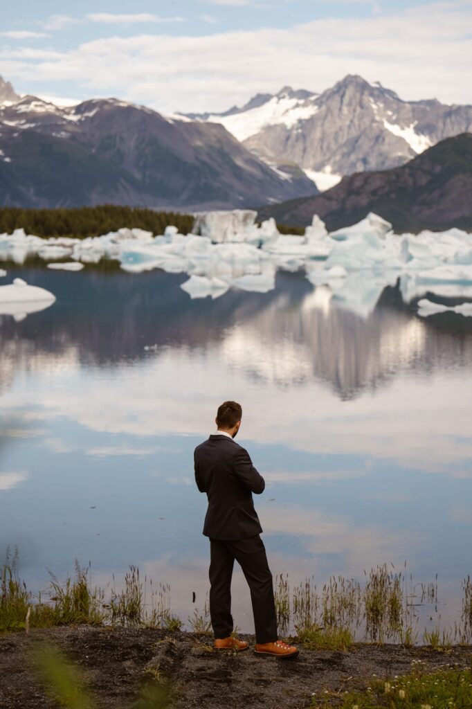 Groom looking out at an Alaskan glacier before his elopement ceremony