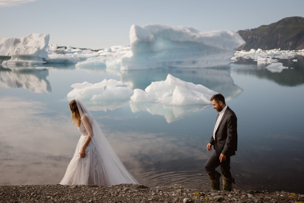 Couple walking on the shore of a glacial lagoon with icebergs in the background