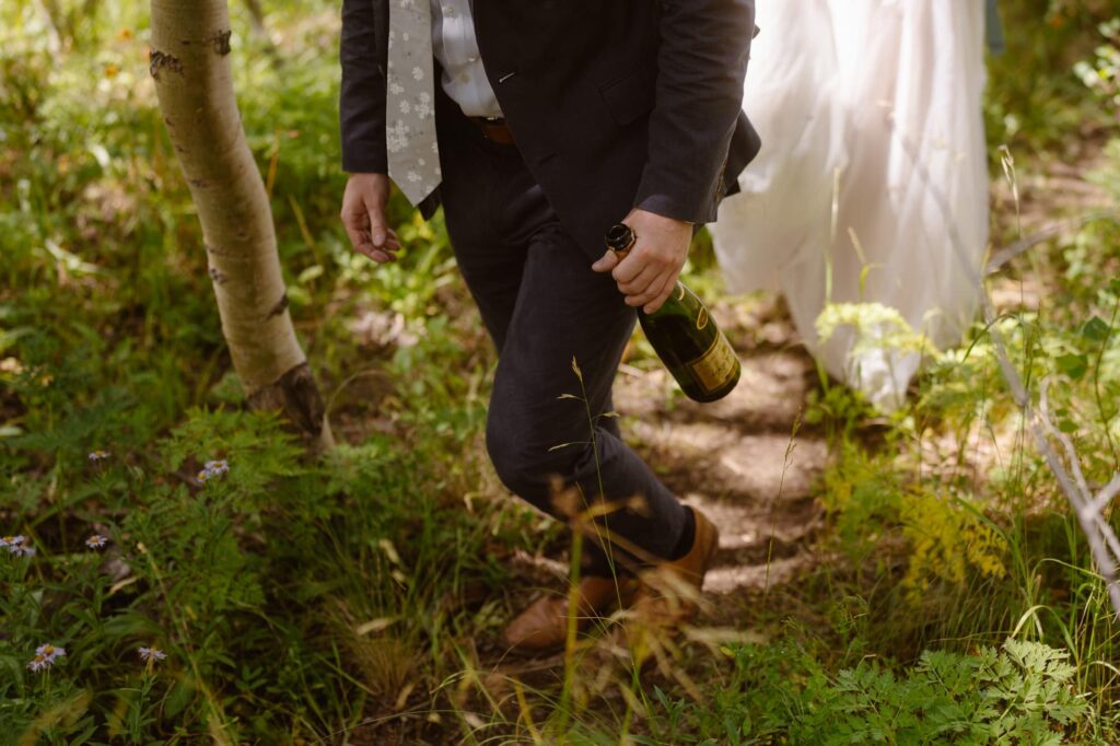 Groom hiking with a bottle of champagne