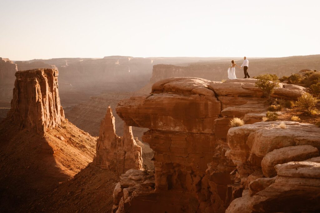 Bride and groom walking to the edge of a cliff during Moab adventure elopement