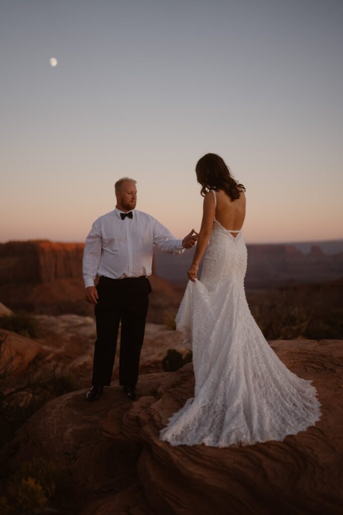 Couple walking down a desert landscape with the moon in the distance