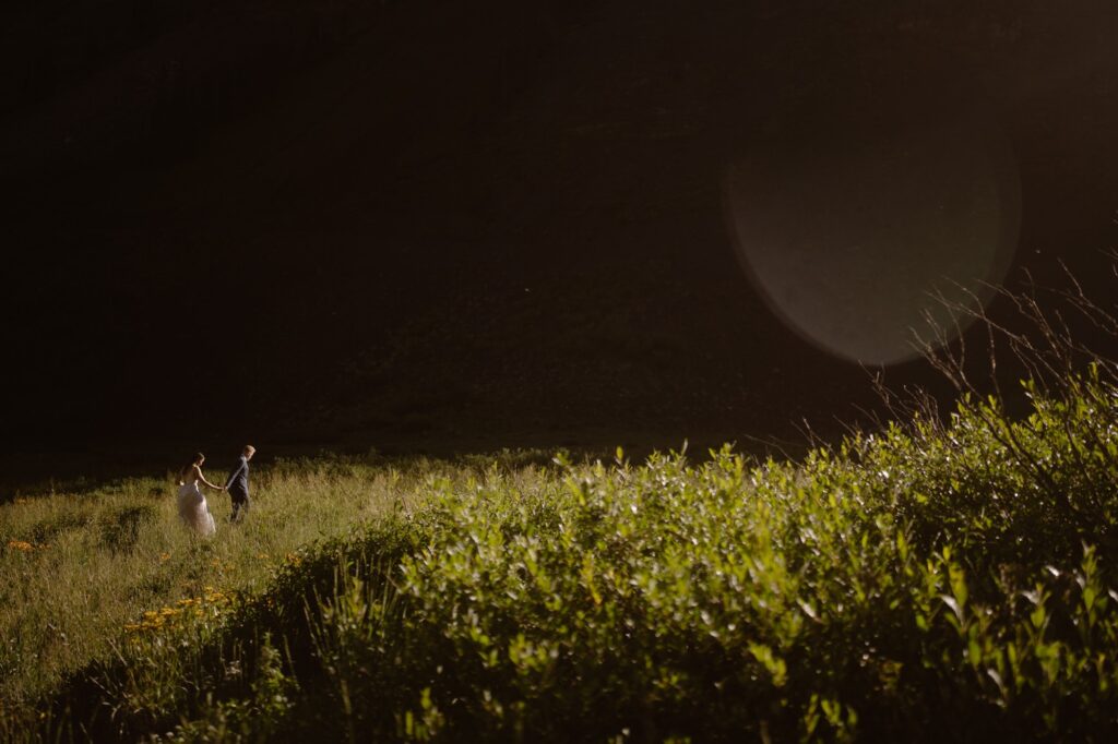 Couple walking through a meadow with dramatic lighting on their elopement day