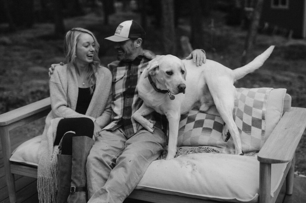 Couple sitting on outdoor furniture and laughing with their dog