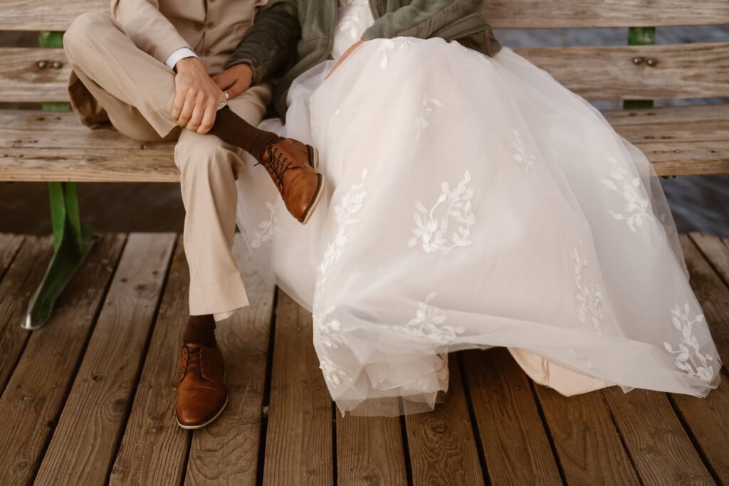 Couple sitting on a bench in their wedding attire down by the lake