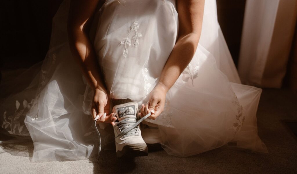 Bride tying her hiking boots underneath her wedding dress
