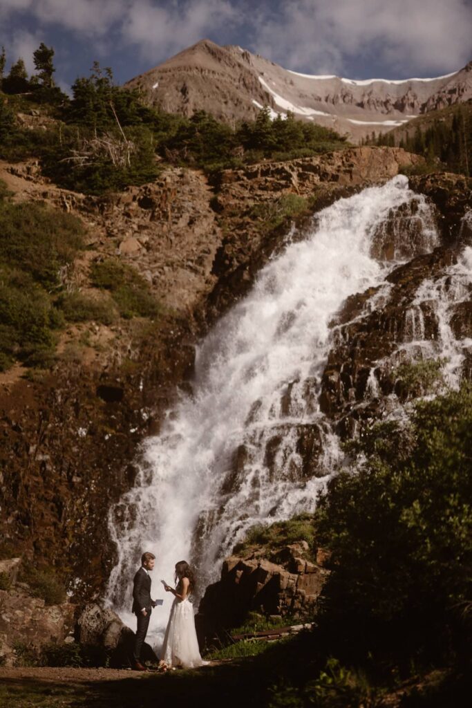 Bride and groom exchanging vows in front of Colorado waterfall