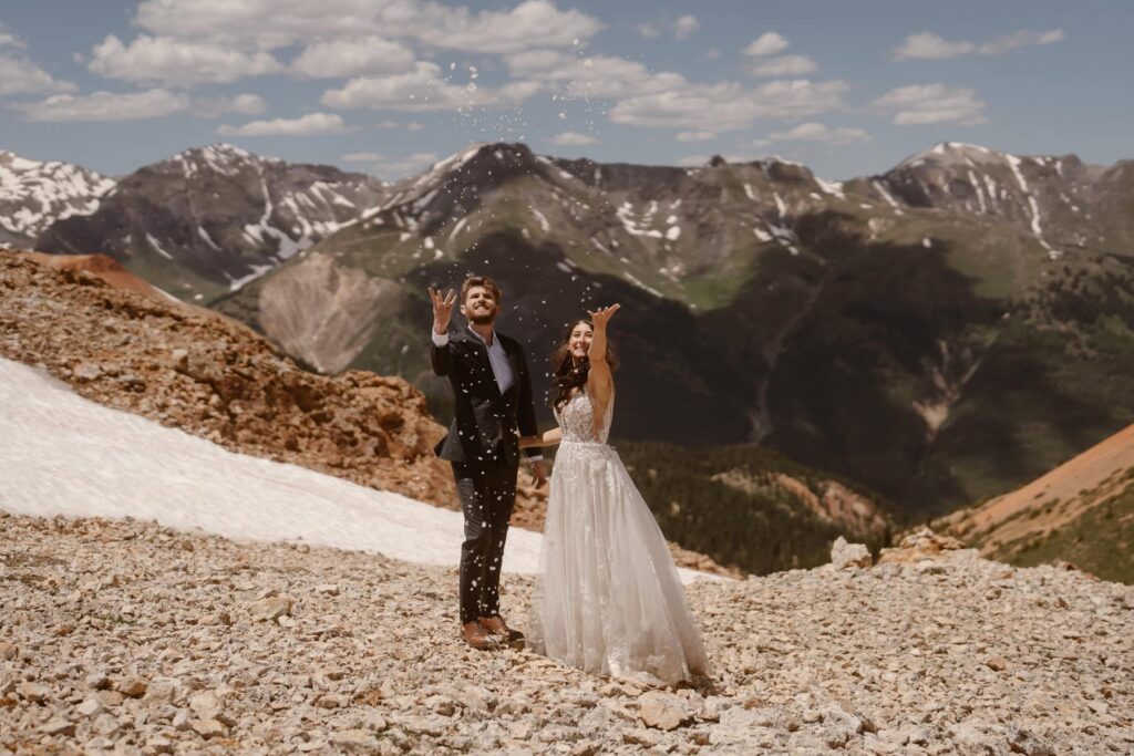 Bride and groom throwing snow in the air on top of a mountain