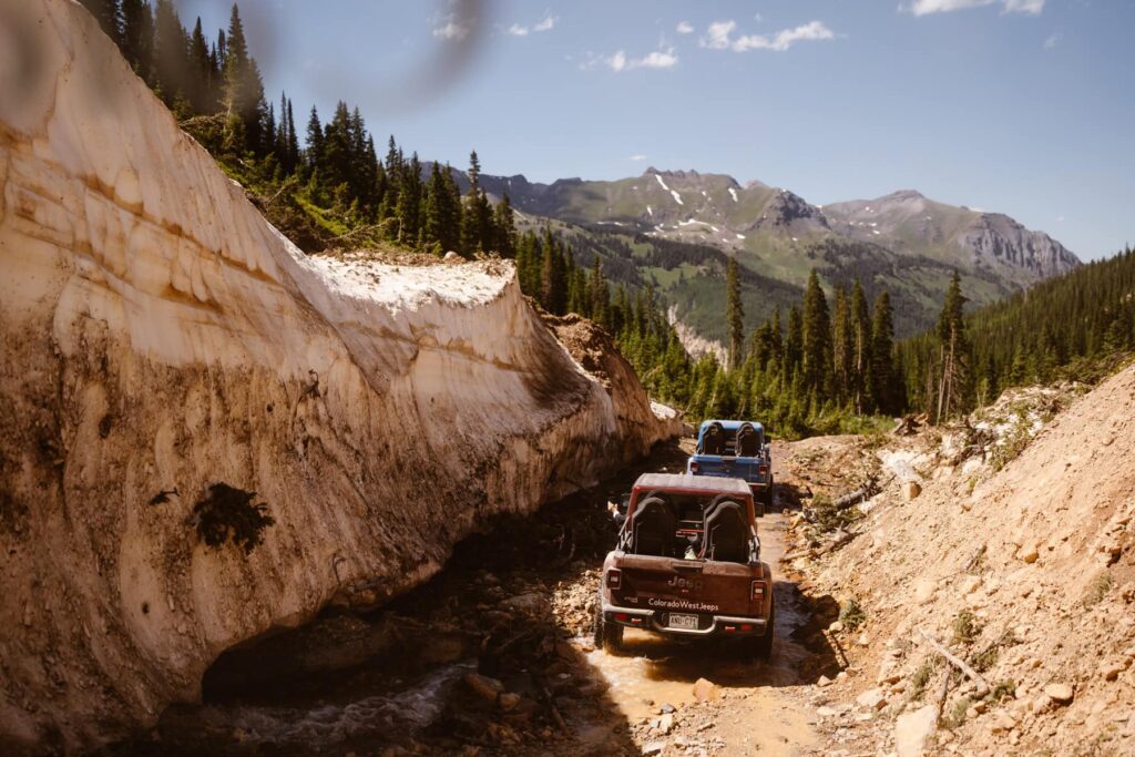 Jeeps driving by a wall of snow in the mountains