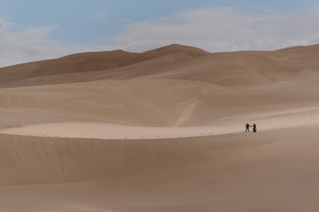 Couple walking across the sand dunes in Colorado on their wedding day wearing all black