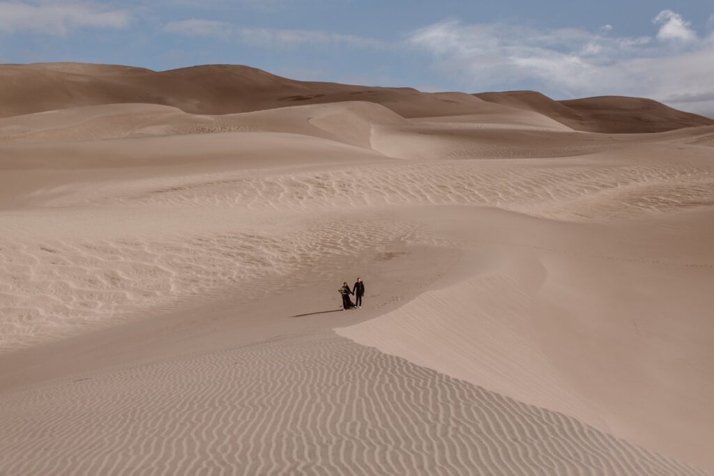 Bride and groom in all black walking across Great Sand Dunes in Colorado