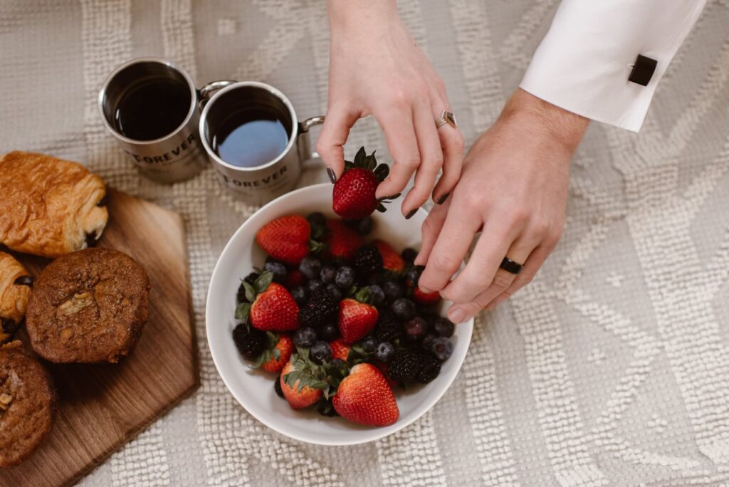 Couple with black wedding rings reaching for fruit bowl after their sunrise wedding