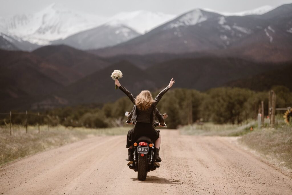 Motorbike wedding in Colorado with couple riding their Triumph bike down a dirt road