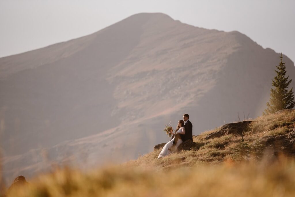 Couple snuggled up on a rock overlooking the mountains on their wedding day