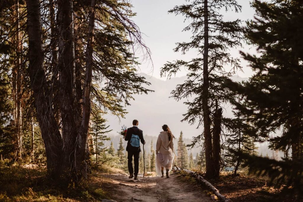 Bride and groom hiking through the trees off toward mountains in the distance