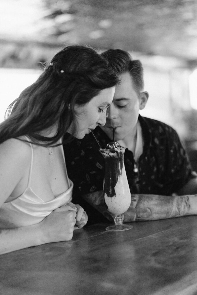 Couple sharing a boozy milkshake at a dive bar on their wedding day