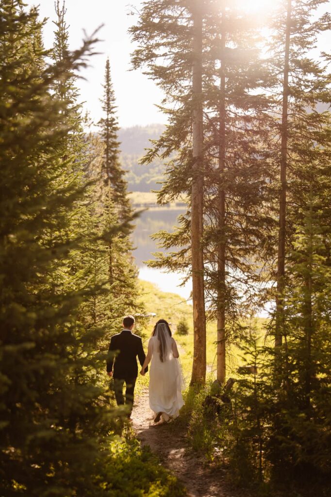 Couple hiking a trail down to the lake in their wedding attire