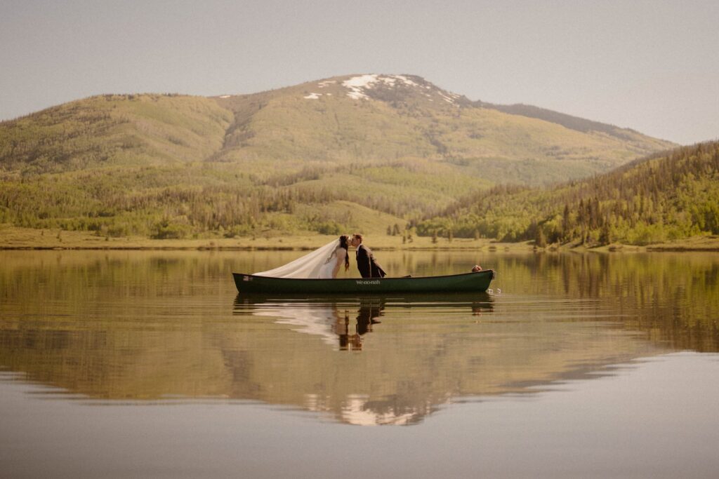 Bride and groom kissing on a canoe with mountains in the background