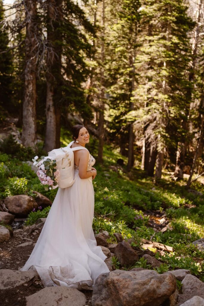 Bride in a white backpack hiking through the woods