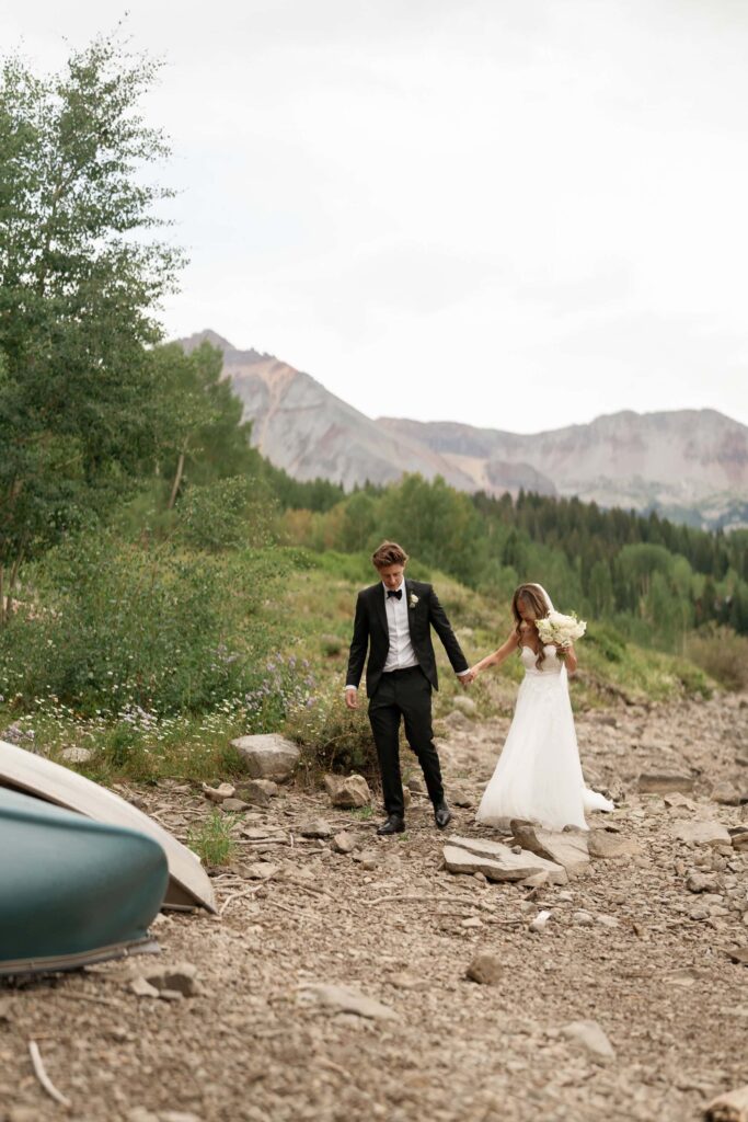 Bride and groom walking down lakeshore in the mountains