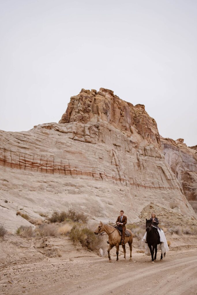 Bride and groom horseback riding through desert at Amangiri