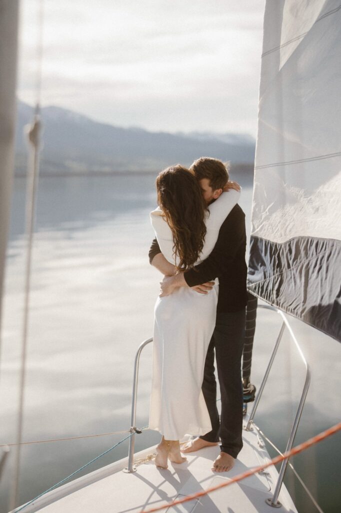 Couple hugging on the bow of a sailboat on glassy water