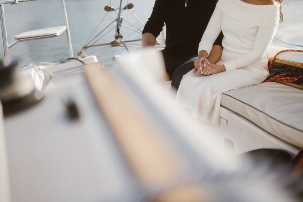 Couple holding hands and steering a sailboat during engagement photoshoot