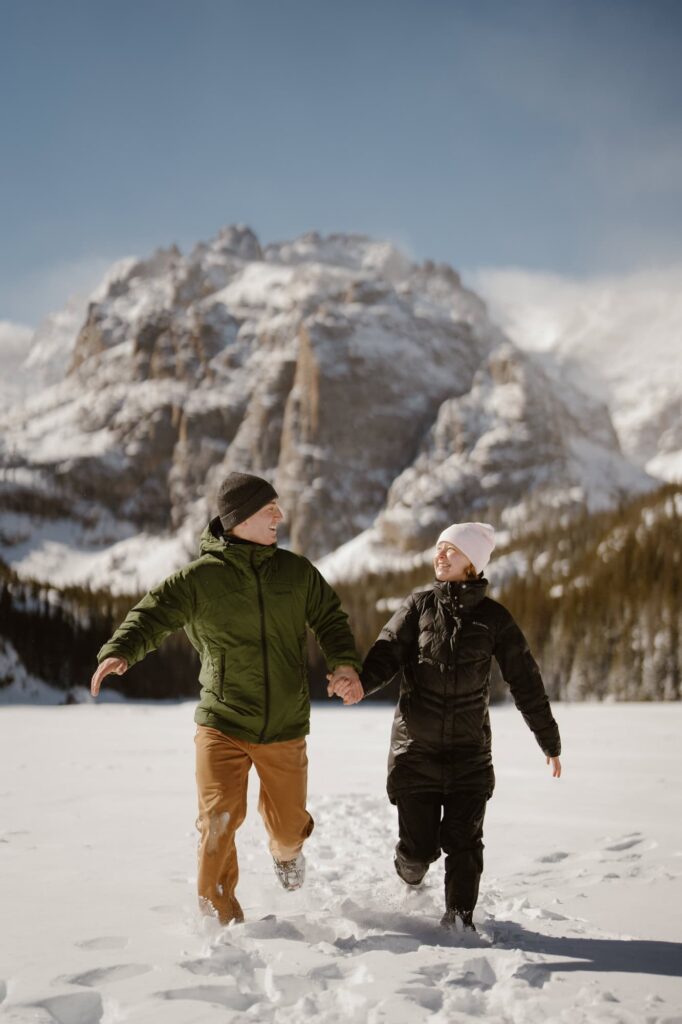 Couple running through the snow in the mountains after a hiking proposal