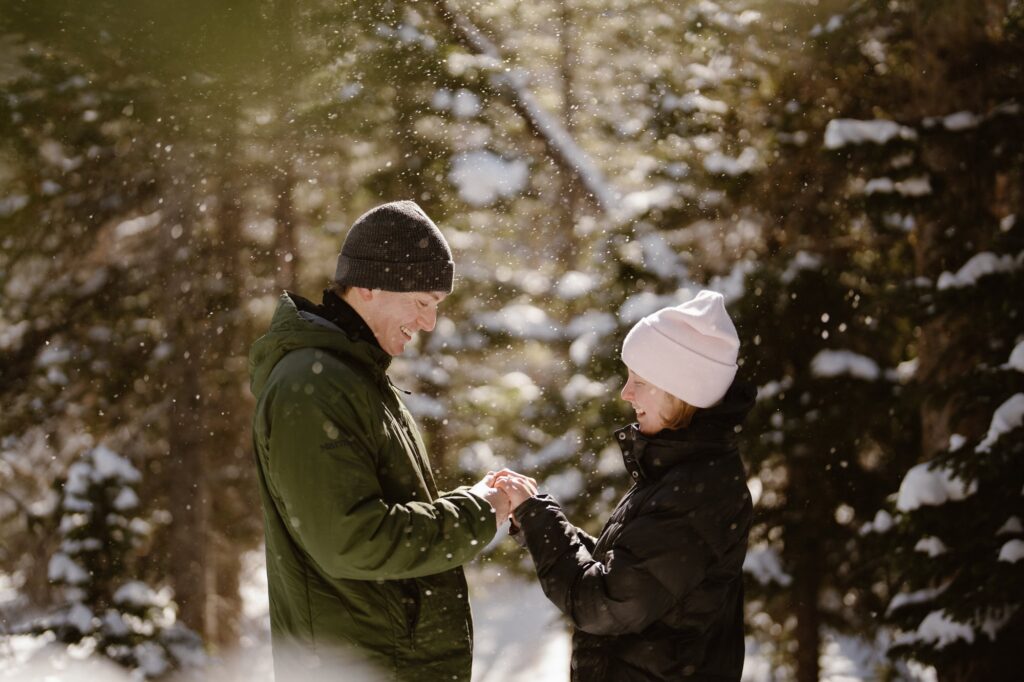 Snow falling around couple in the forest after surprise hiking proposal