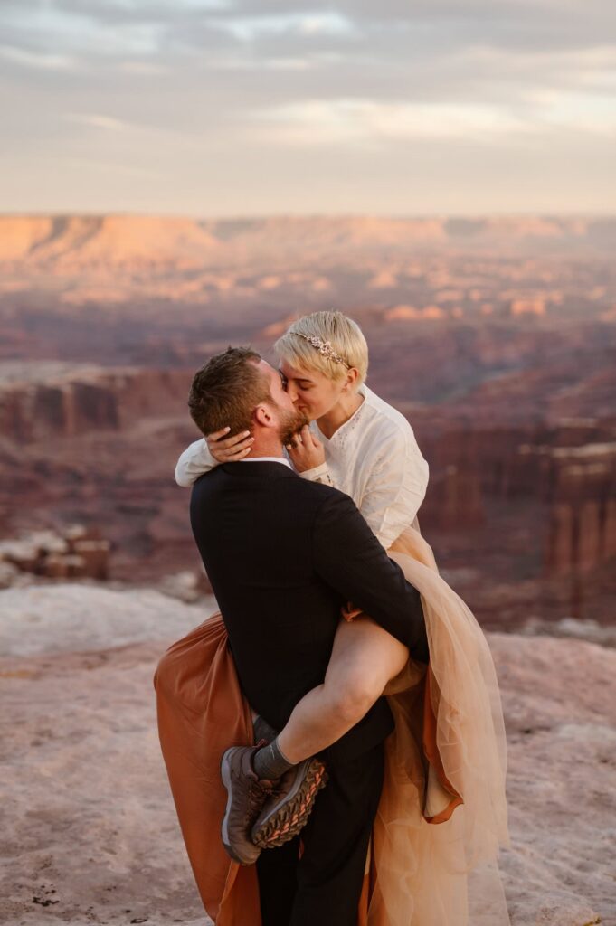 Groom picking bride up at the edge of a cliff