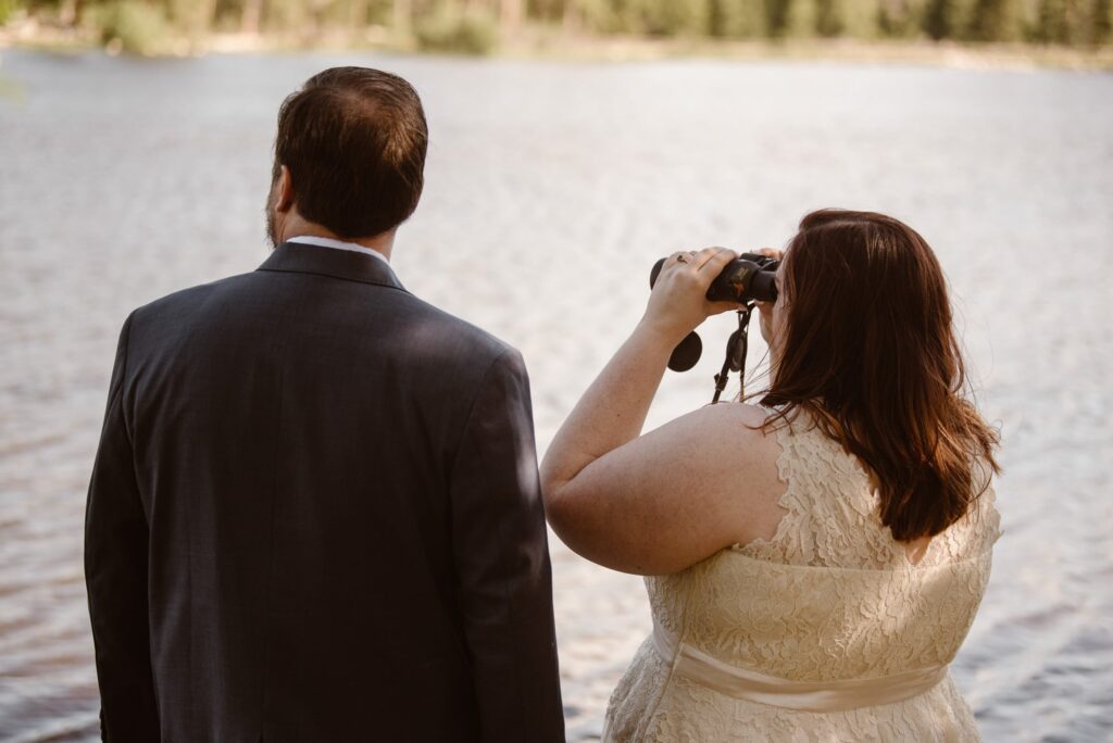 bride and groom looking through binoculars at mountain lake