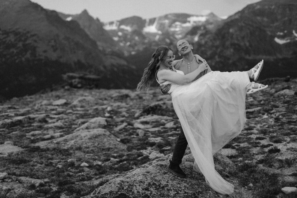 black and white photo of a groom picking up a bride on top of a mountain