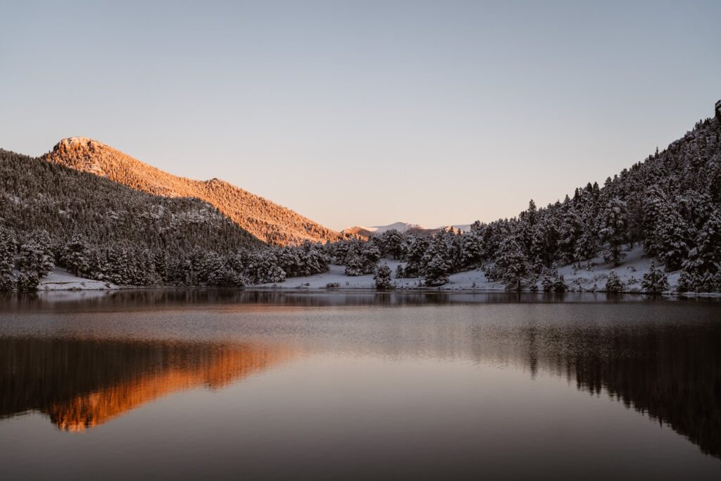 View of snow covered mountains and a calm lake at sunrise in Rocky Mountain National Park at Lily Lake wedding ceremony site