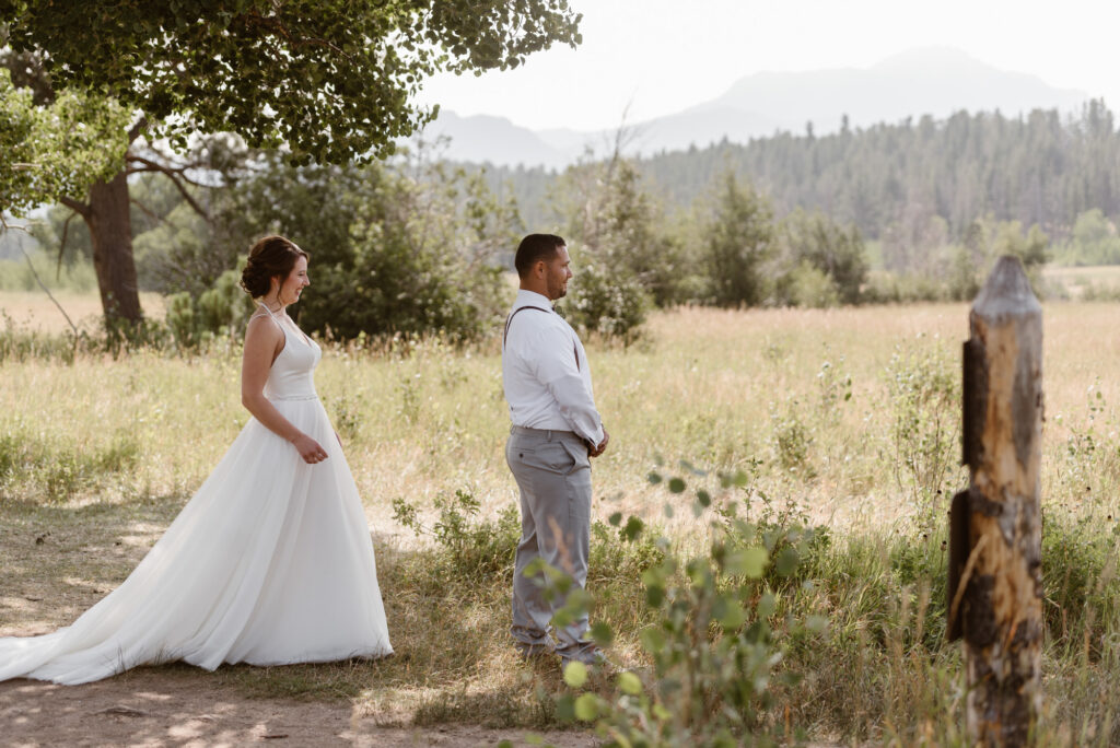 Bride and groom about to share their first look on the edge of Upper Beaver Meadows with mountains in the distance