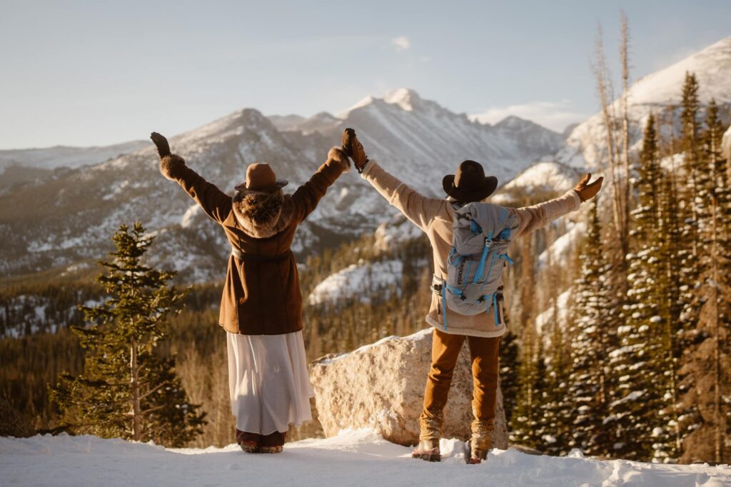 Couple with hands in the air overlooking the sunlit mountains in Estes Park