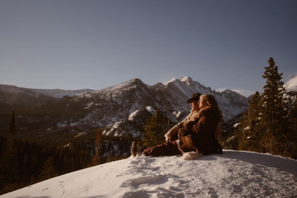 Couple sitting at overlooking, looking off into the sun with snowy mountains in the distance
