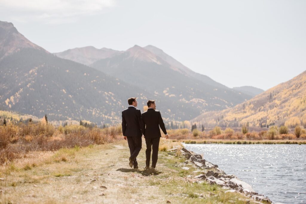 grooms walking along a lake with mountains in the background