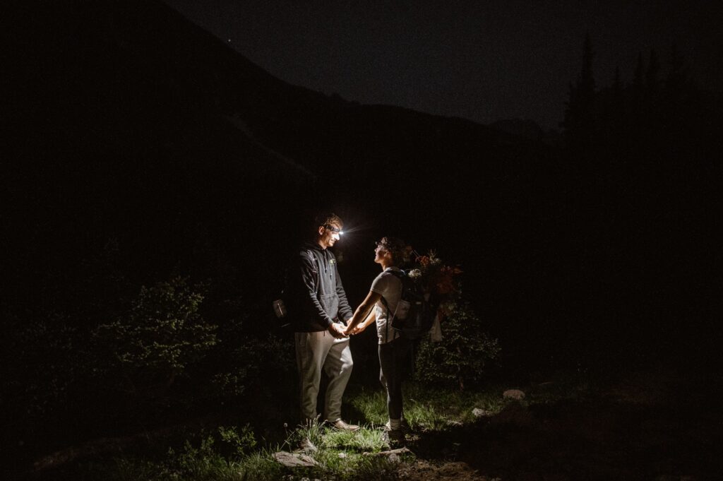 couple hiking a mountain in the dark to get married at sunrise at a mountain lake