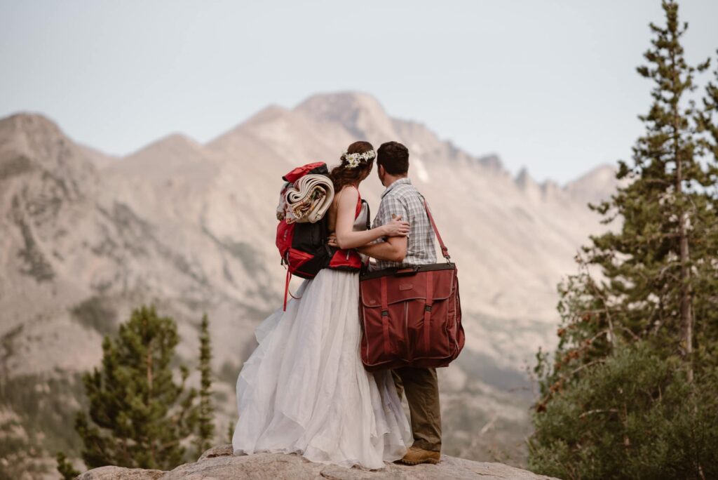 Bride and groom with backpacks on looking at the mountains