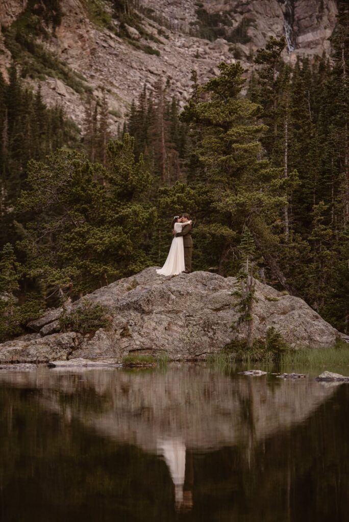 Bride and groom on a rock with lake reflection