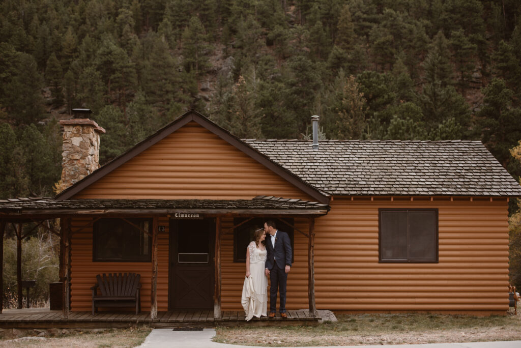 Couple standing in front of the Rockmount Cottages on their wedding day in Estes Park