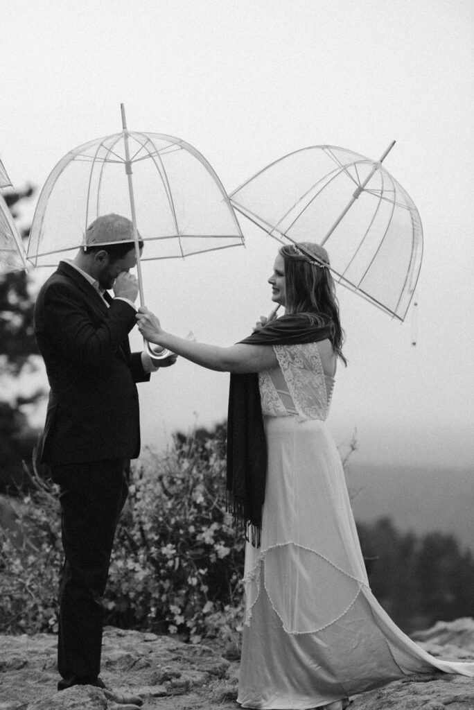 Black and white photo of couple under umbrellas exchanging vows