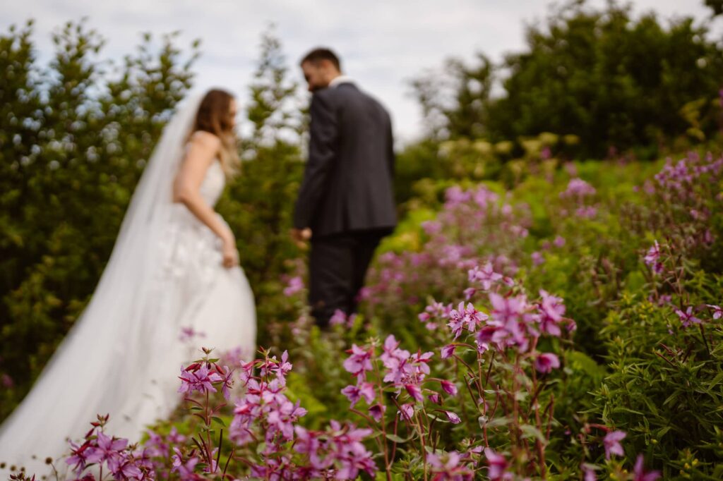 Bride and groom walking through pink wildflowers in Alaska