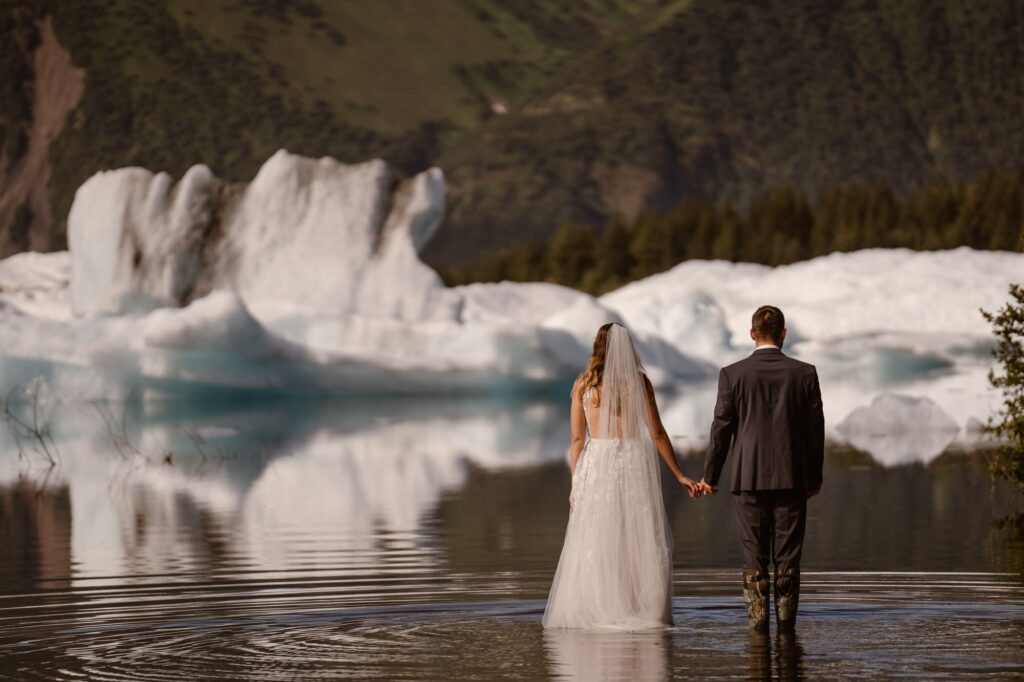 Bride and groom standing in a glacial lagoon in Alaska