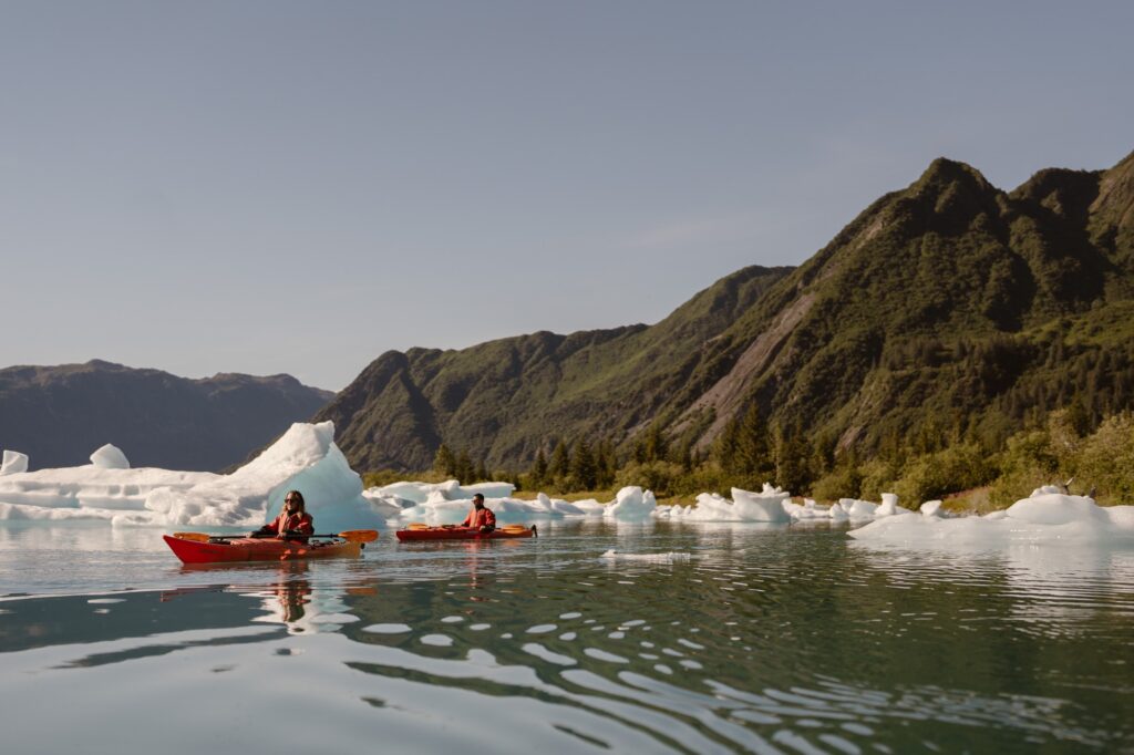 View of icebergs, kayaks, and mountains in Bear Glacier