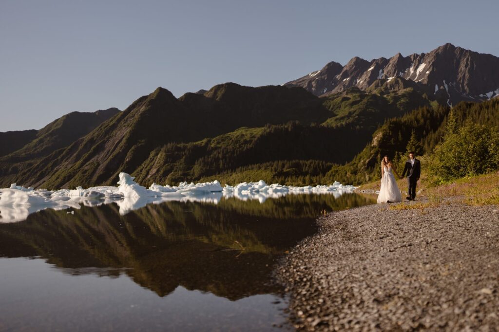 Couple walking down the shore of Bear Glacier during helicopter elopement in Alaska