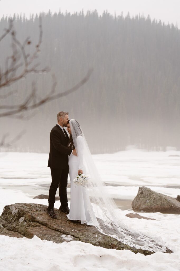 Couple standing on a rock at snow covered Bear Lake elopement