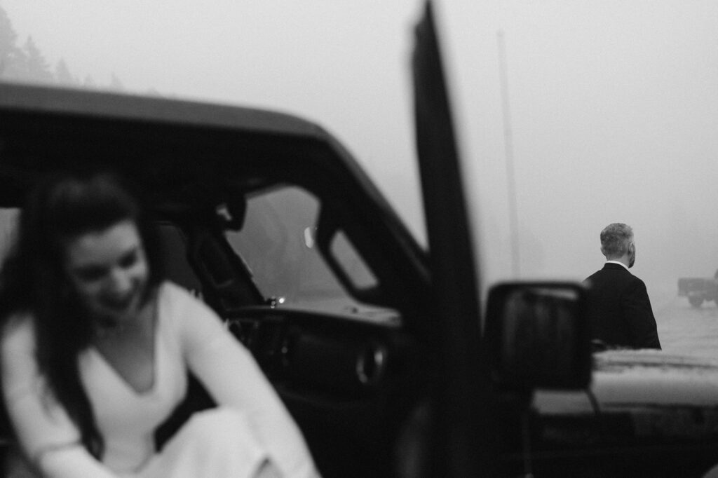 Bride getting ready in a Jeep while groom looks off in the distance