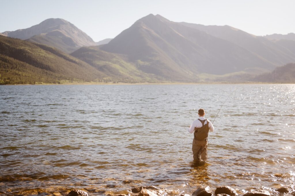 Groom fly fishing at a mountain lake in Colorado during his adventure elopement
